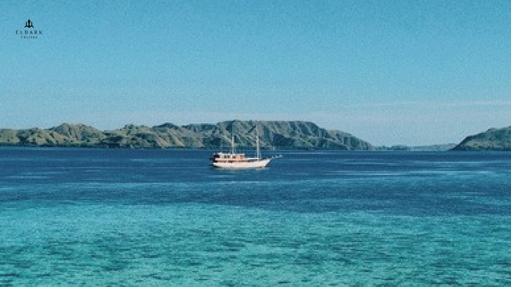 A Phinisi cruise sailing in calm Labuan Bajo waters under bright August skies